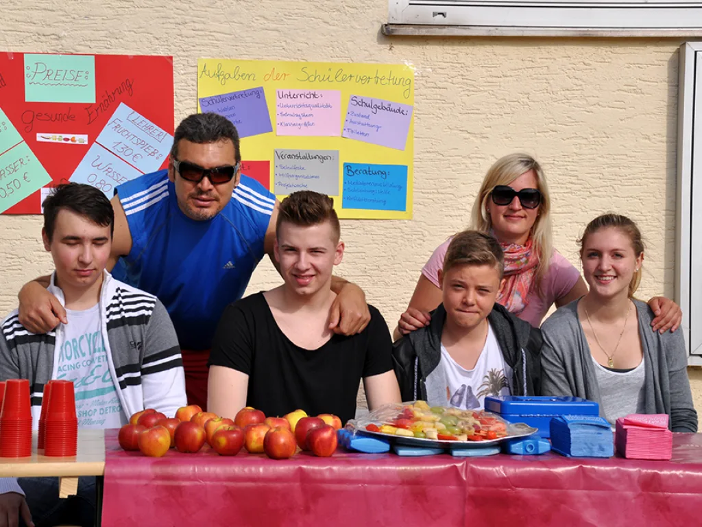 Gruppe steht hinter einem Tisch mit Obst und Getränken.